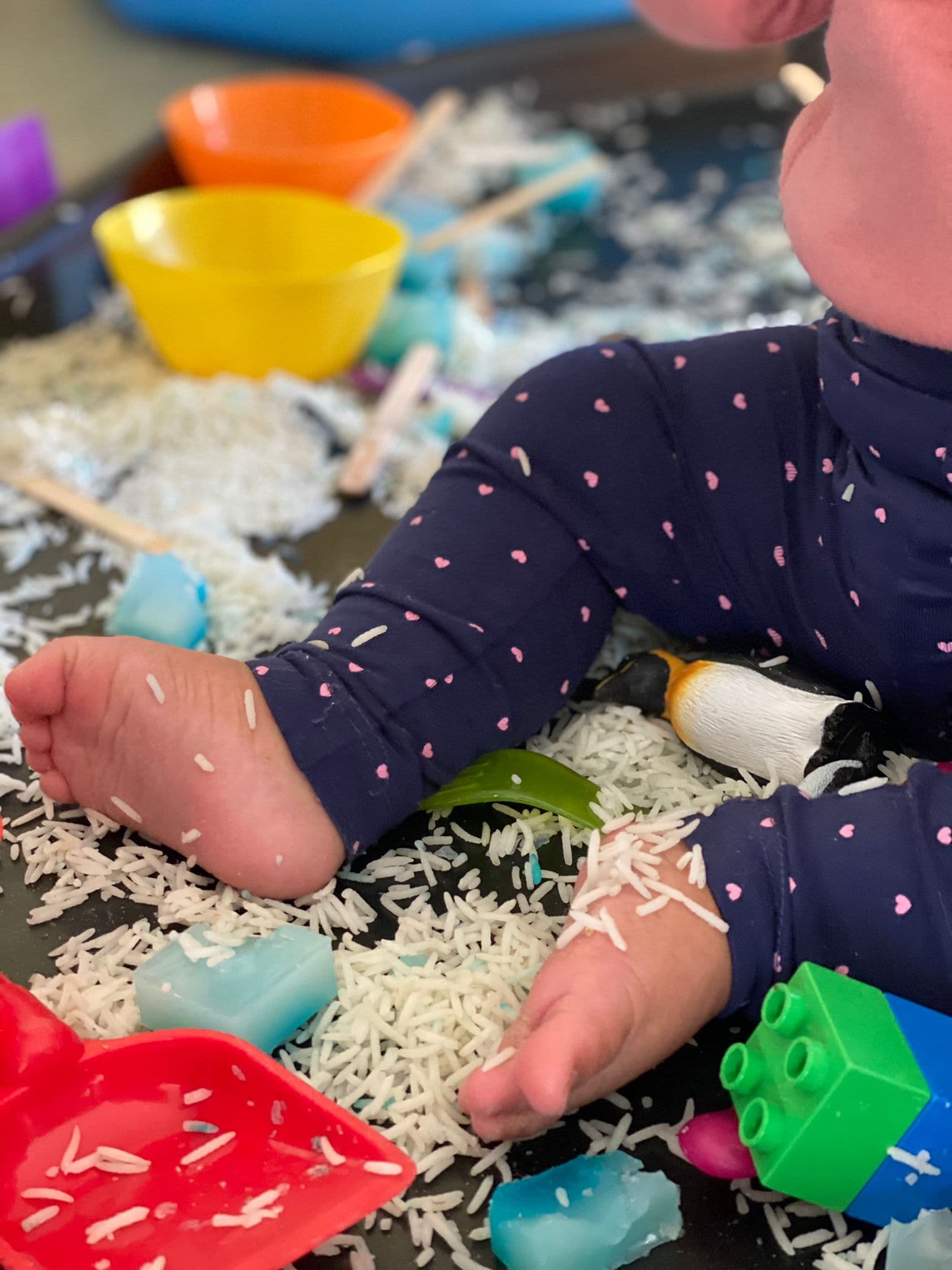 A child exploring coloured rice and toys at a Happy MOMents sensory play session